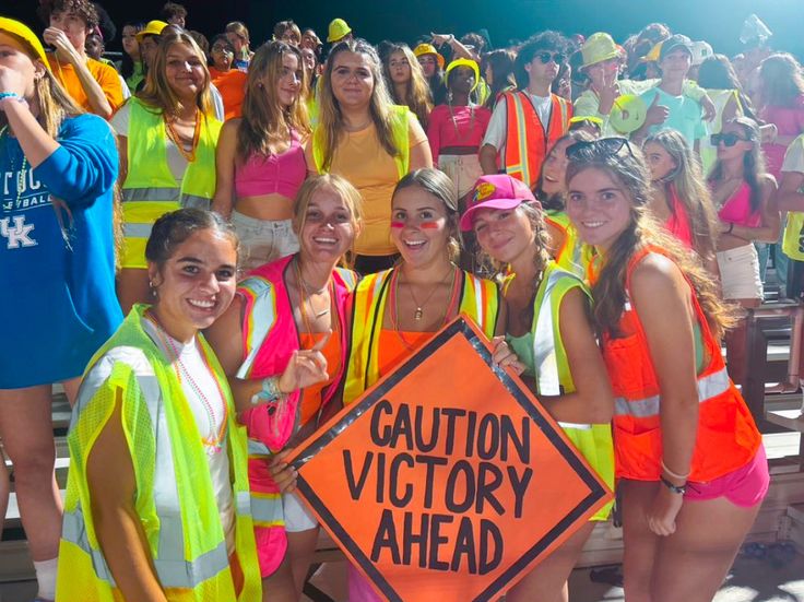 a group of young women standing next to each other in front of a crowd wearing neon vests