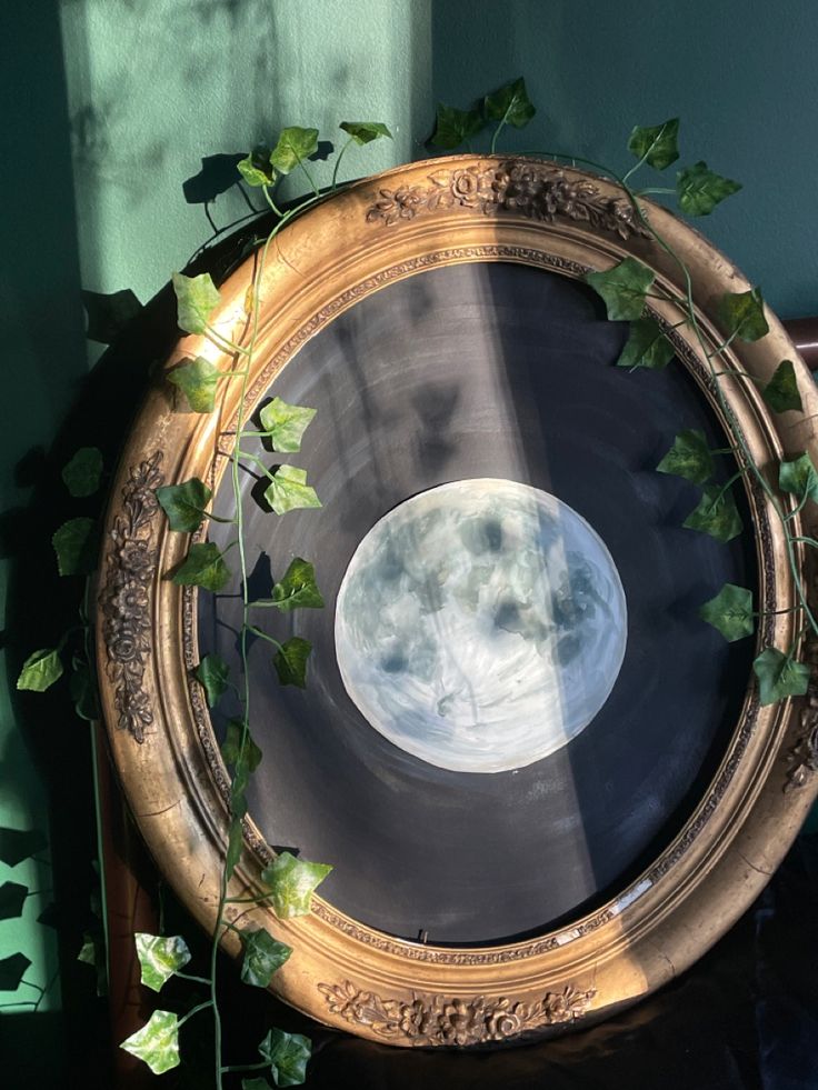 a gold framed mirror with ivy growing on it's sides and the moon in the center