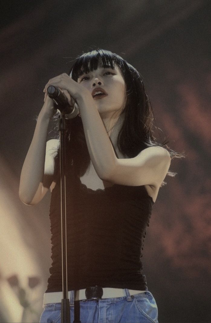 a woman in black shirt and jeans holding a microphone up to her face while standing on stage