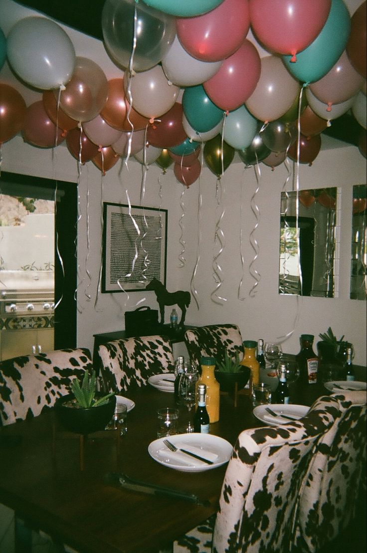 a room filled with lots of balloons and plates on top of a wooden dining table