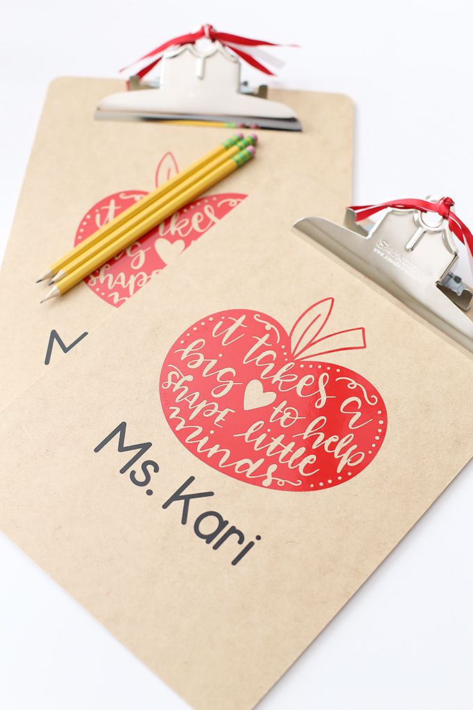 a clipboard with an apple on it next to a pair of scissors and pencils