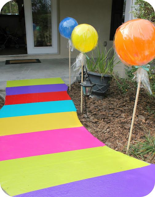 an outdoor walkway made out of colored paper with balloons on sticks in front of it