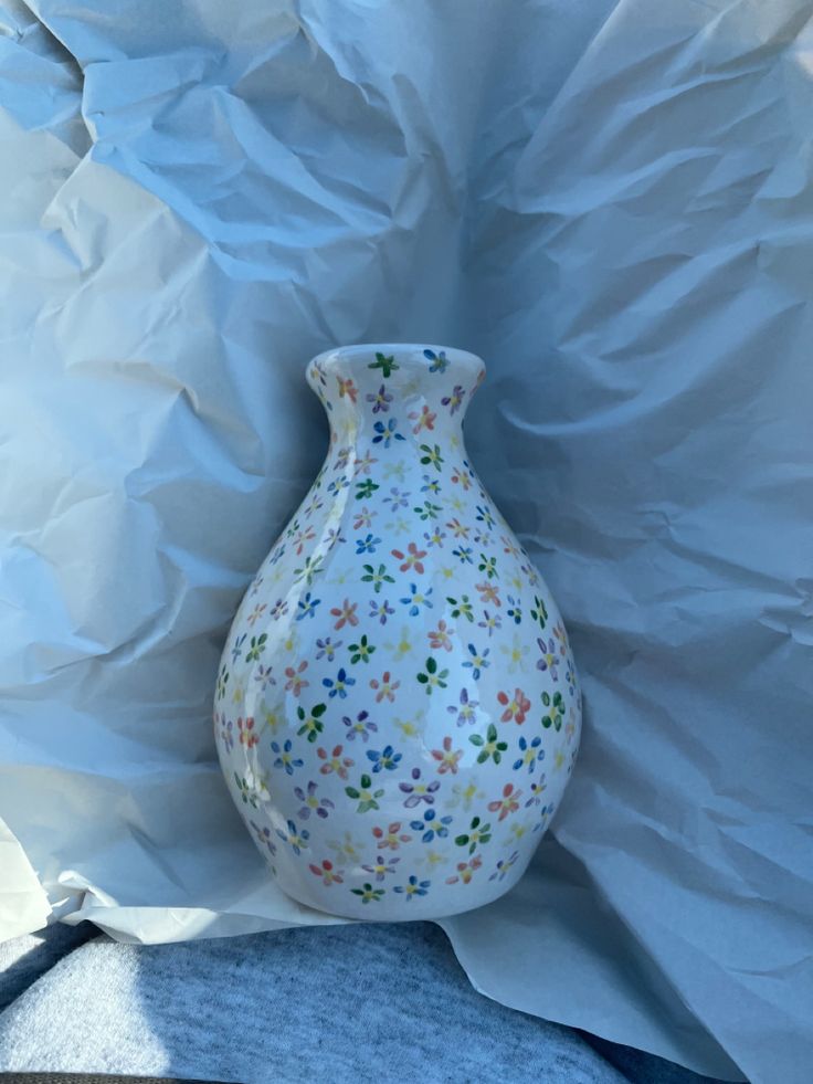 a white vase with multicolored flowers on it sitting in front of a sheet of paper