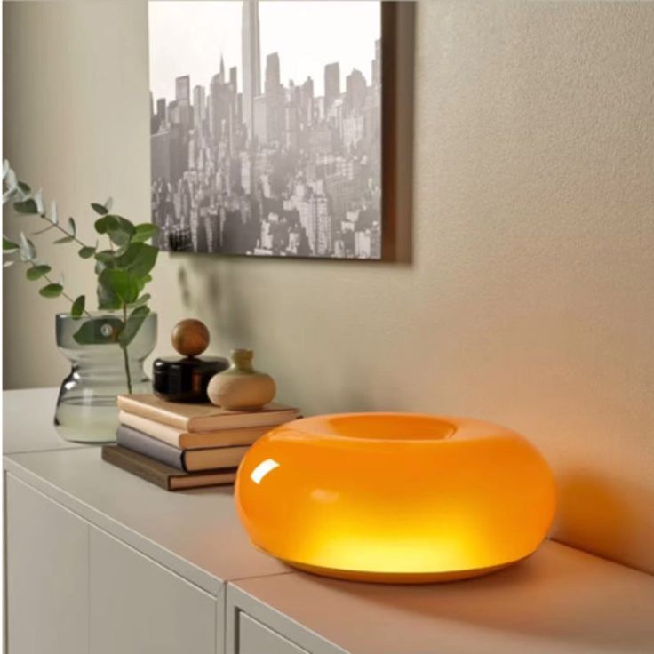 an orange bowl sitting on top of a white counter next to a plant and books