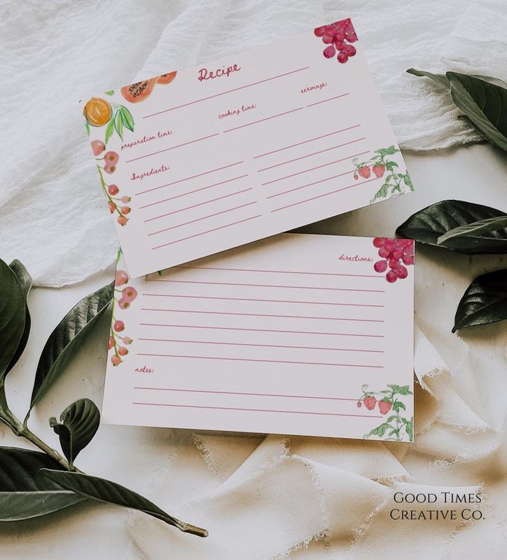 two notepads sitting next to each other on top of a white sheet with leaves