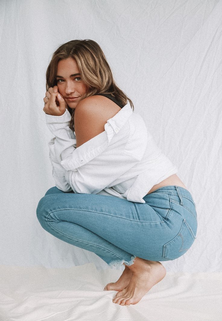 a woman in white shirt and jeans kneeling on bed