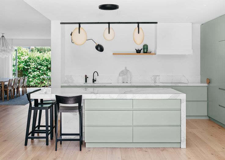 a kitchen with an island and bar stools in it, along with three lights hanging from the ceiling