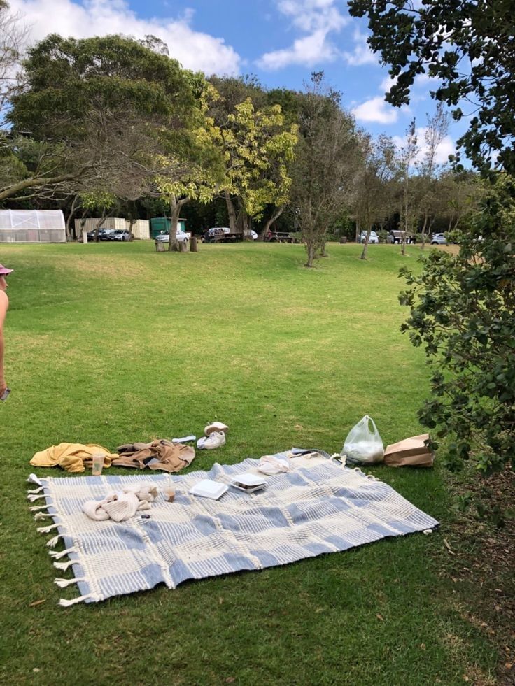 a woman standing next to a picnic blanket on top of a lush green park field