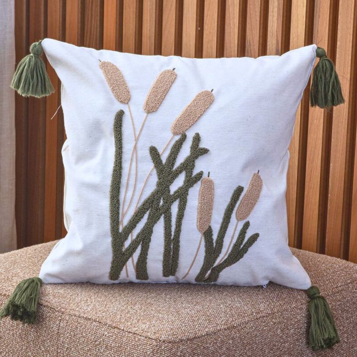 a white pillow with green plants on it sitting on top of a chair next to a wooden wall