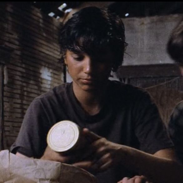 two people sitting at a table with some food in front of them and one person holding a paper plate