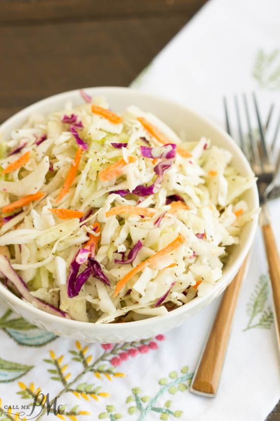 a white bowl filled with coleslaw and carrots next to two silverware