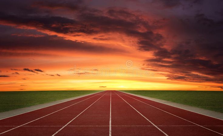 an empty running track with the sun setting in the background and clouds above it,