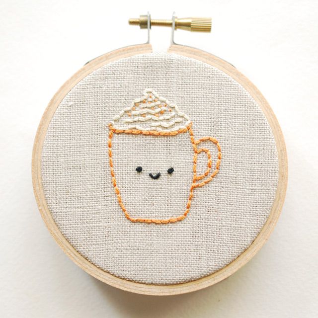 a close up of a embroidery on a hoop with a cup of coffee in it