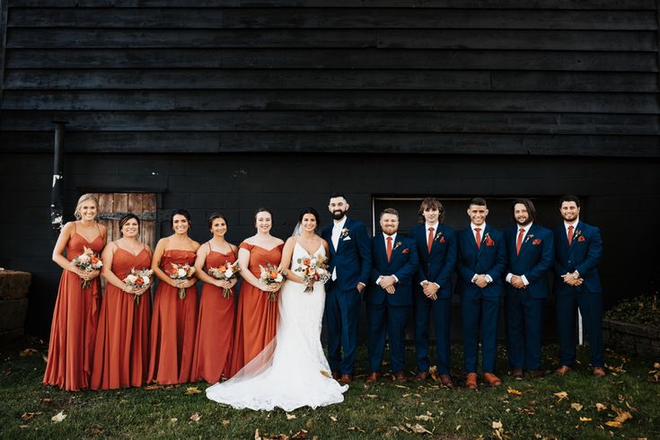 a group of people standing next to each other in front of a black building wearing orange dresses