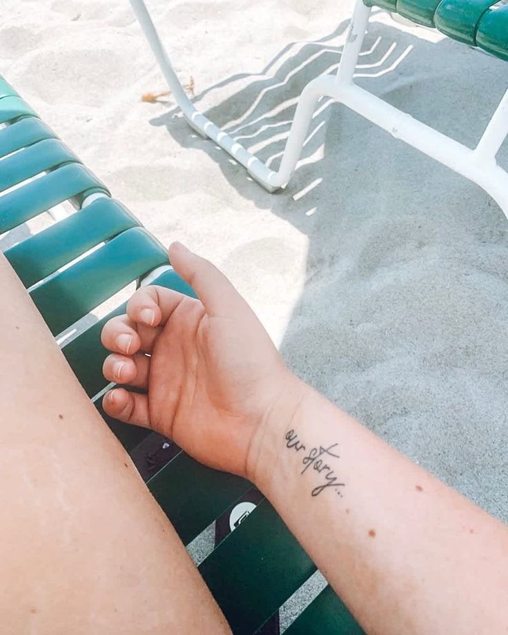 a person with a small tattoo on their arm sitting in a chair at the beach