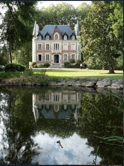 a large house sitting on top of a lush green field next to a lake in front of a forest