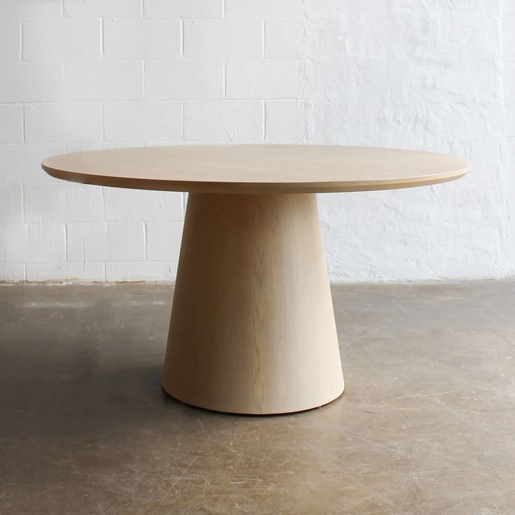 a round wooden table sitting on top of a cement floor next to a white brick wall