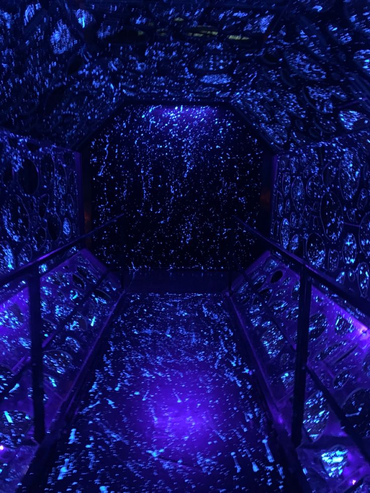 the inside of a tunnel with blue lights and stars on the walls, as well as glass railings