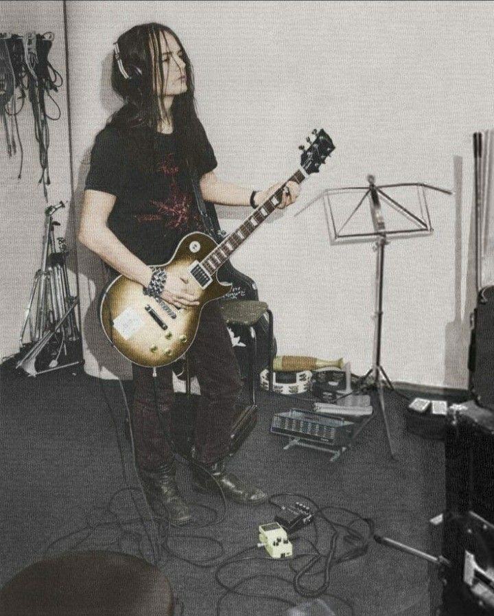 a man with dreadlocks playing an electric guitar in a recording studio, while another musician stands behind him