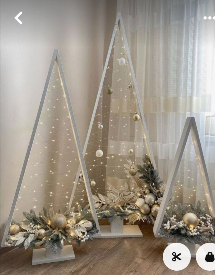 three christmas trees with ornaments on them in front of a window