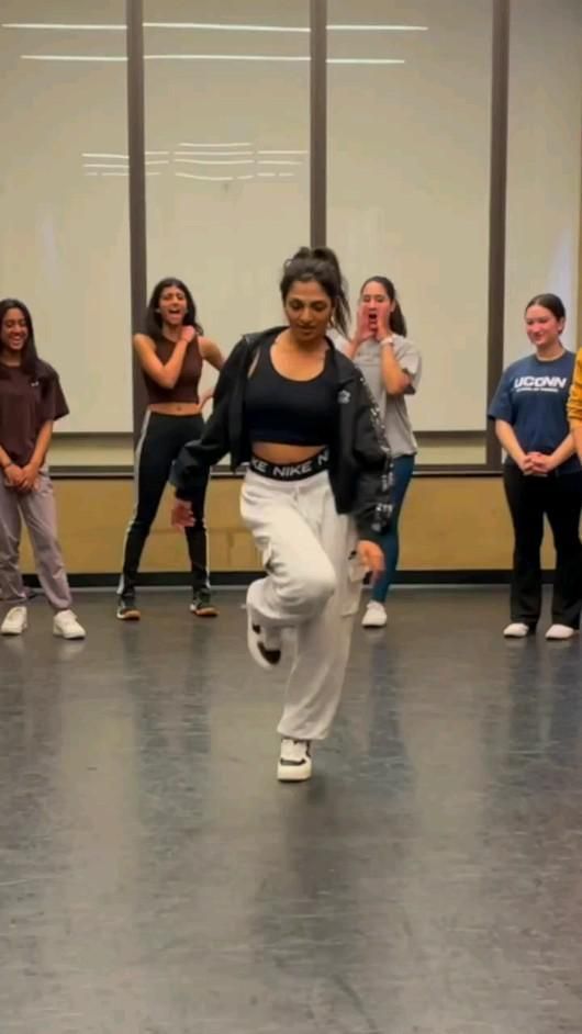 a group of young people standing around each other in a dance studio with one woman dancing