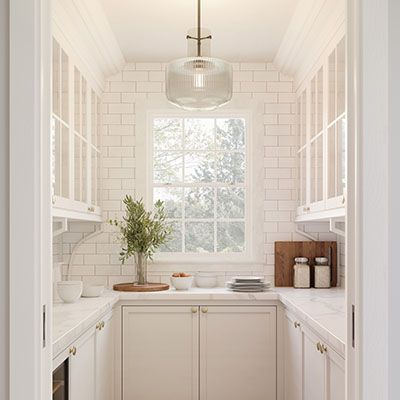 a kitchen with white cabinets and counter tops in front of a window that has a potted plant on it