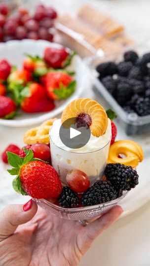 a person holding a bowl full of fruit and yogurt in front of other bowls