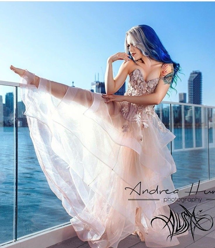 a woman with blue hair is standing on a balcony next to the water and wearing a dress