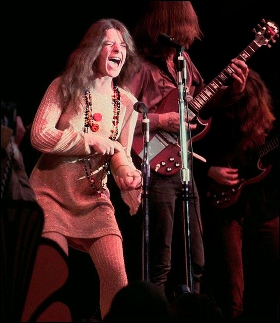 a woman singing into a microphone while standing next to a man with a guitar on stage