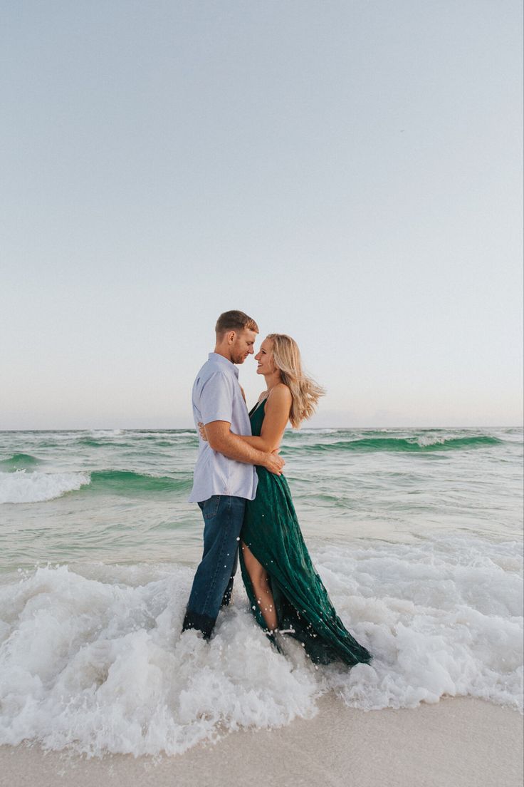 a man and woman standing in the surf at the beach with their arms around each other