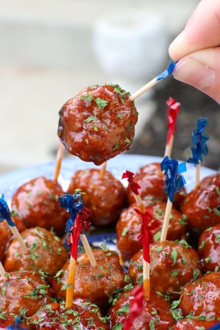 a hand holding a skewer of meatballs with toothpicks in it