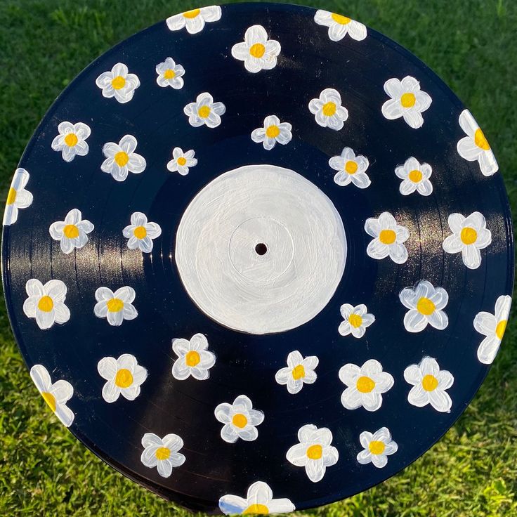 a black and white frisbee with flowers painted on the side, sitting in grass