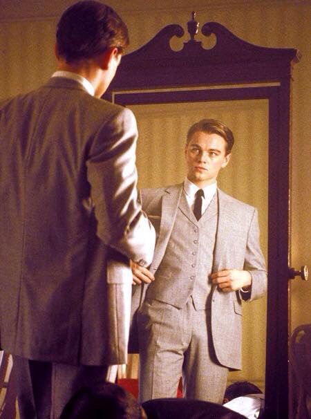 a man standing in front of a mirror wearing a suit and looking at his tie