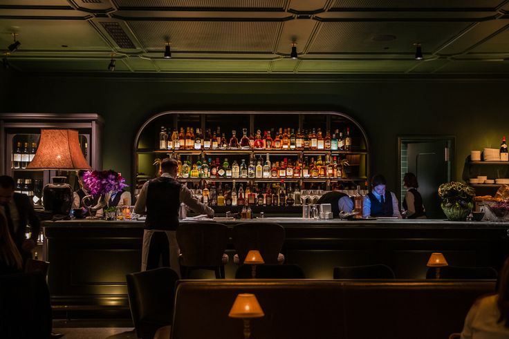 a bar with people sitting at it and some bottles on the shelves in front of them