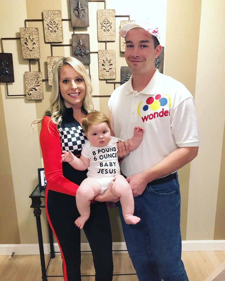 a man and woman holding a baby in front of a wall with pictures on it