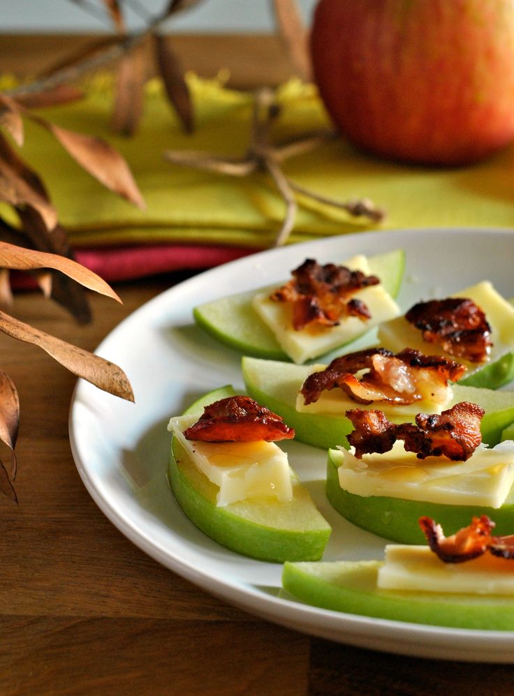 apples with bacon are on a white plate next to an apple and some other fruit