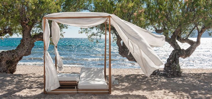 a canopy bed sitting on top of a sandy beach next to the ocean and trees