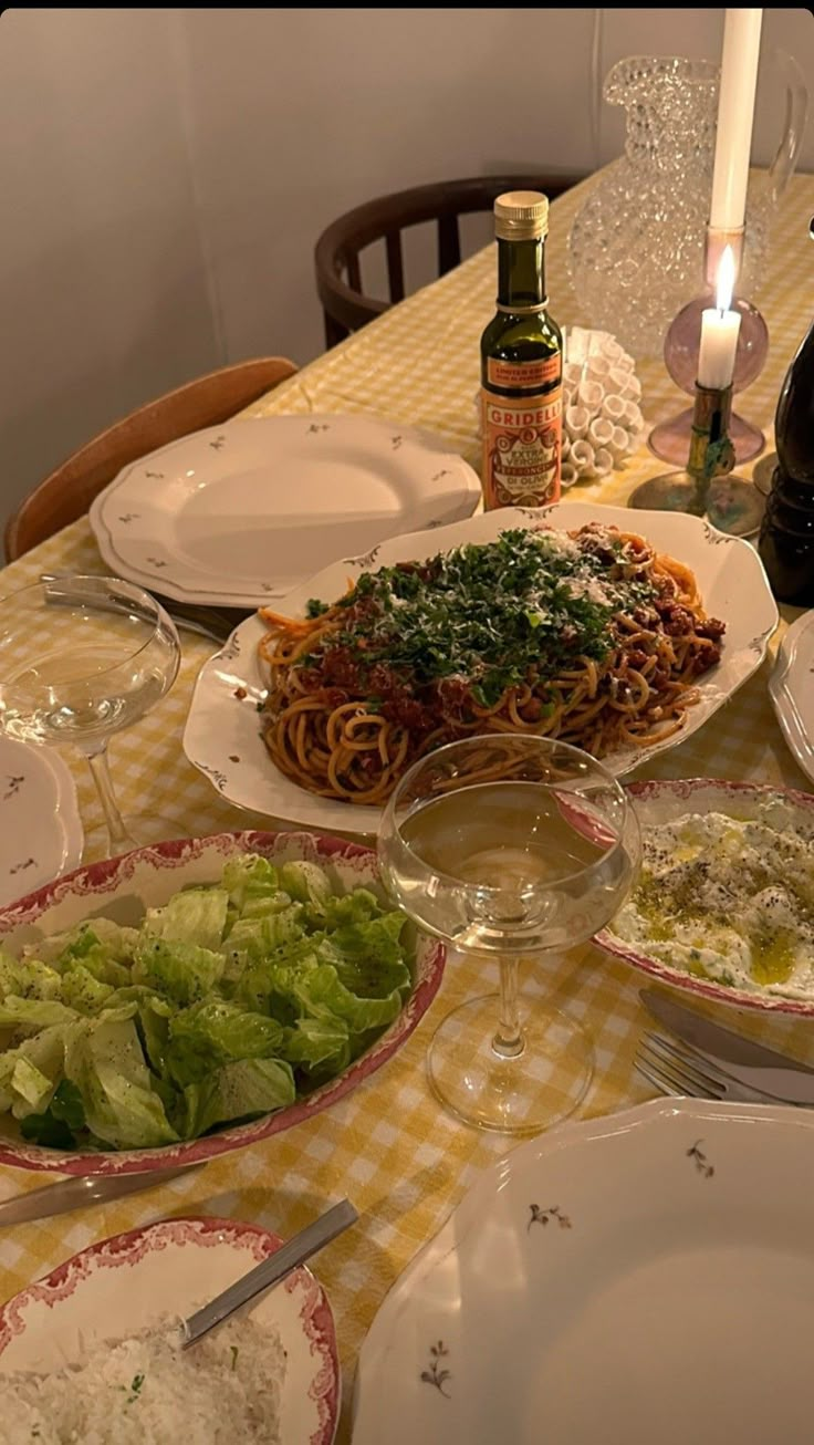 the table is set with many plates and bowls of food, wine bottles, and utensils