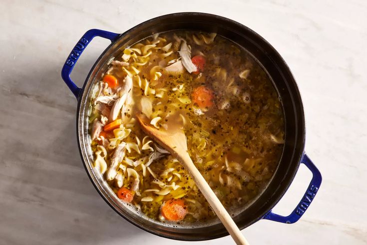 a pot filled with soup and vegetables on top of a white counter next to a wooden spoon