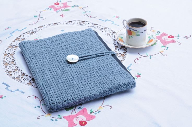 a blue crocheted notebook sitting on top of a table next to a cup of coffee