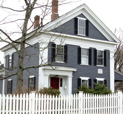 a white picket fence in front of a blue house with black shutters and red door