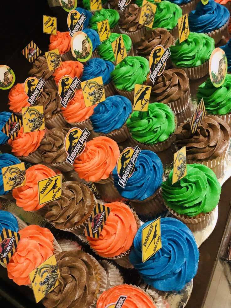 many cupcakes with different colors and designs are on display for sale in a store