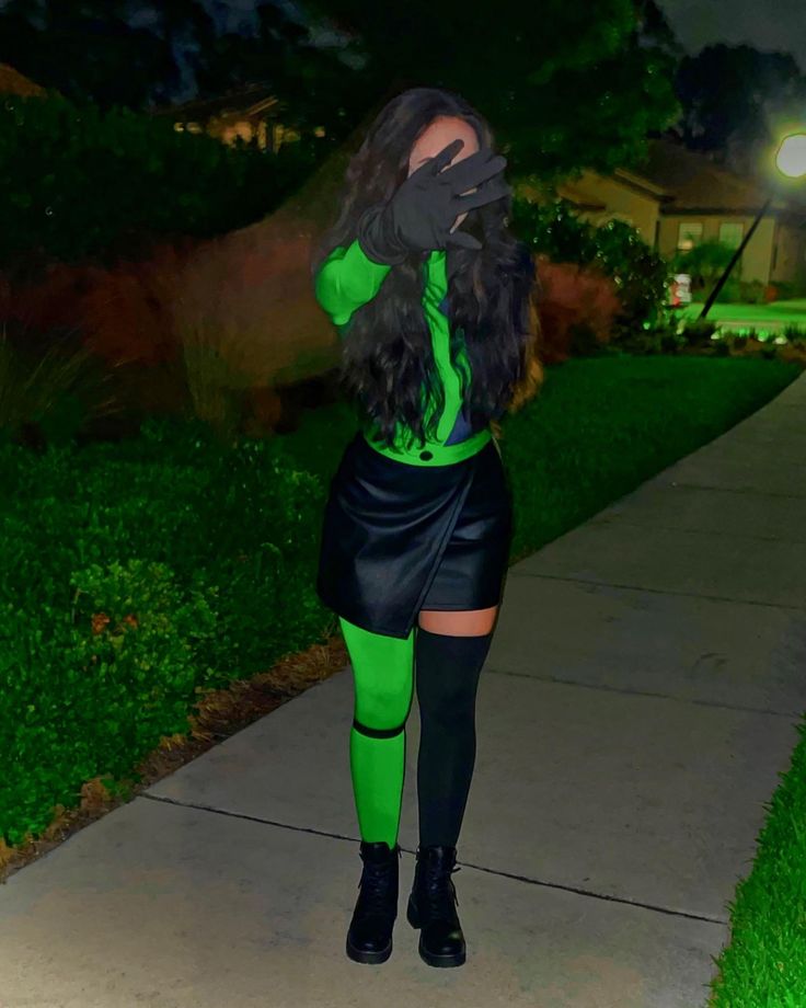 a woman dressed in green and black posing for the camera on a sidewalk at night