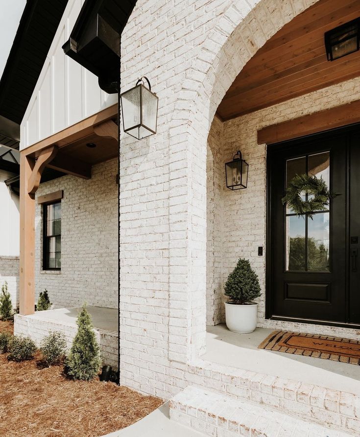 a white brick house with a black front door and two planters on the porch