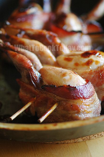 bacon wrapped chicken on skewers in a skillet