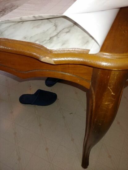 a wooden table with a marble top and blue shoes on the floor next to it