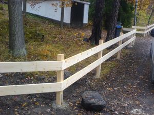 a car parked on the side of a road next to a wooden fence and trees