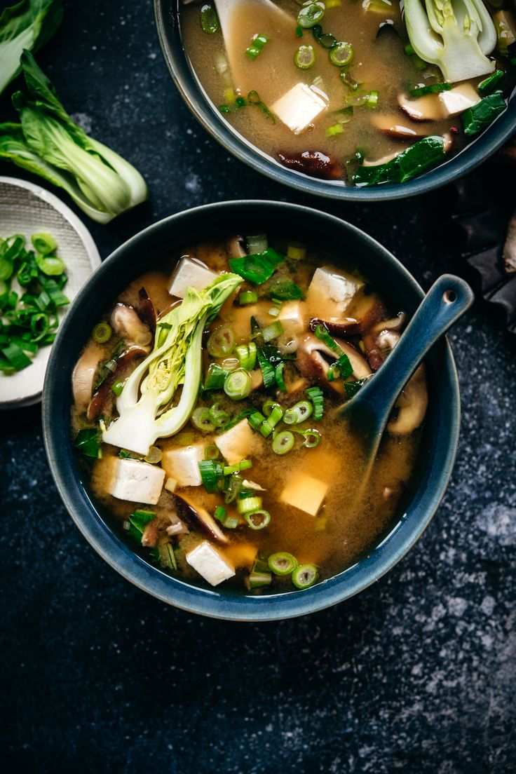 two bowls filled with soup and vegetables on top of a black table next to other dishes