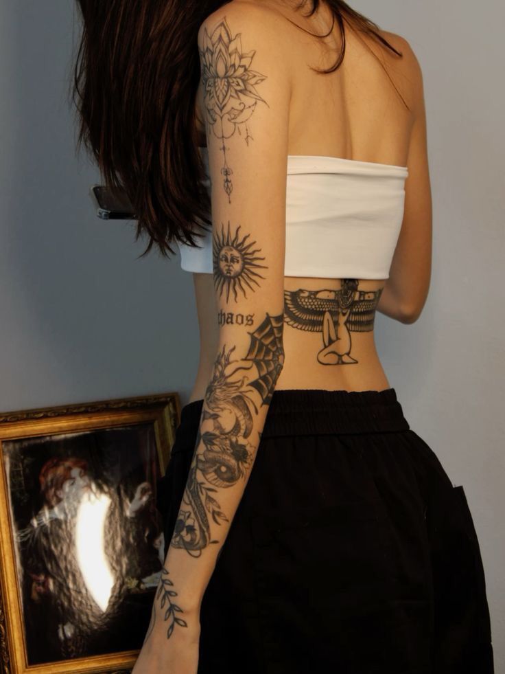 a woman with tattoos on her arm and shoulder standing in front of a framed photograph