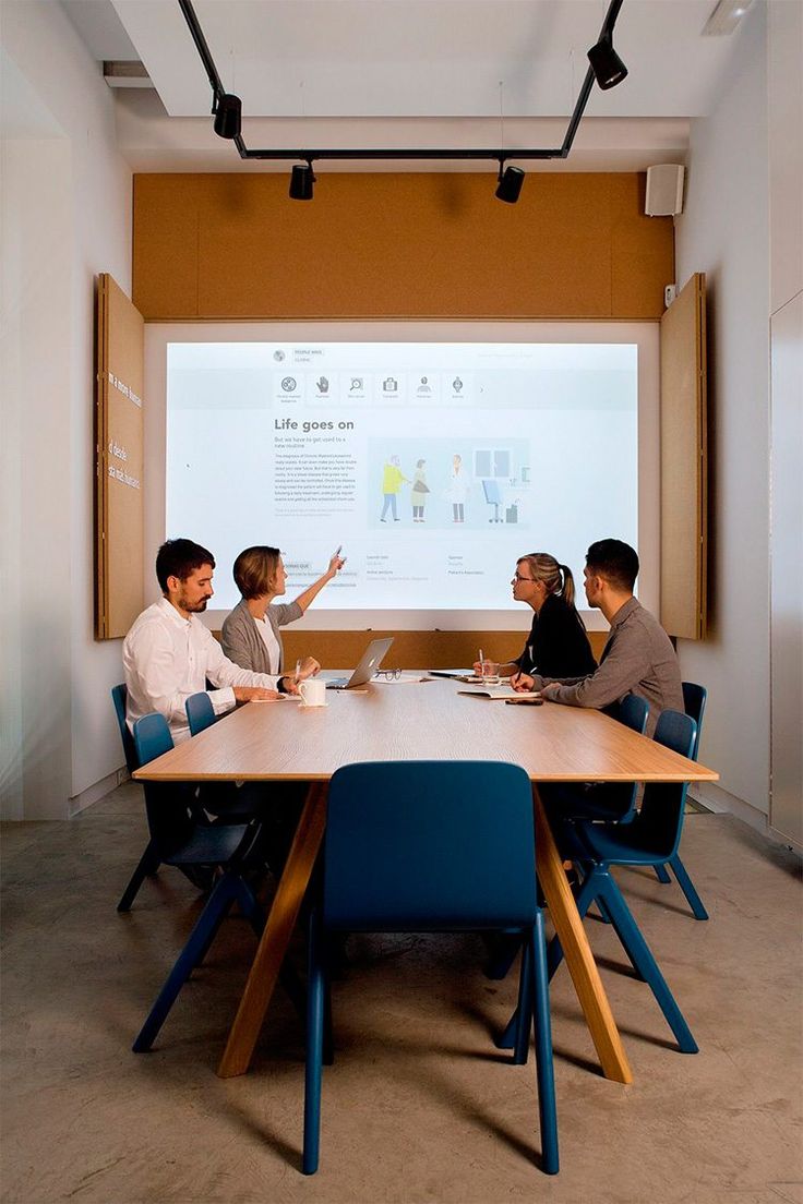 three people sitting at a table in front of a projector screen with a presentation on it